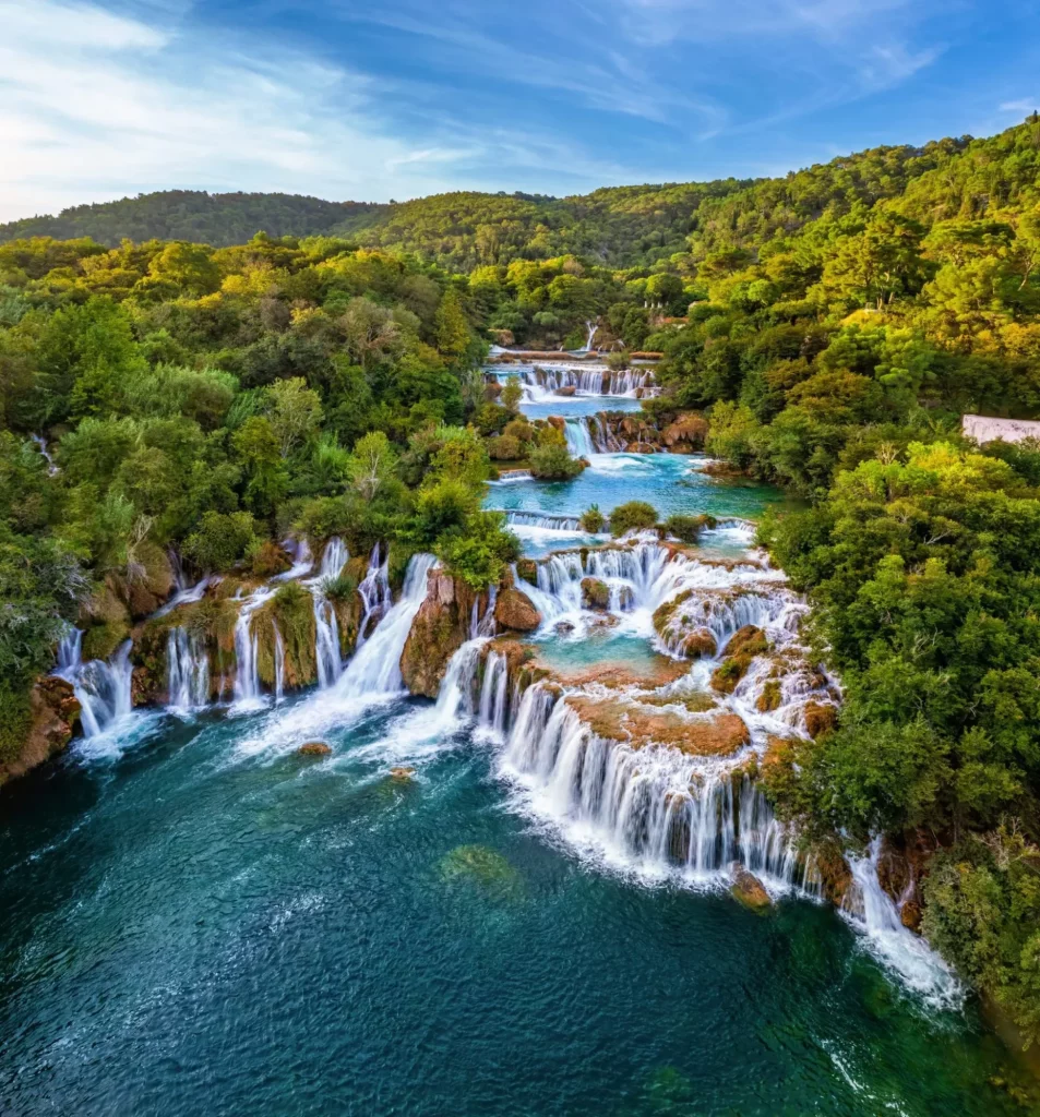 Krka, Kroatien - Luftaufnahme der wunderschönen Krka-Wasserfälle im Krka-Nationalpark an einem hellen Sommermorgen mit grünem Laub, türkisfarbenem Wasser und blauem Himmel