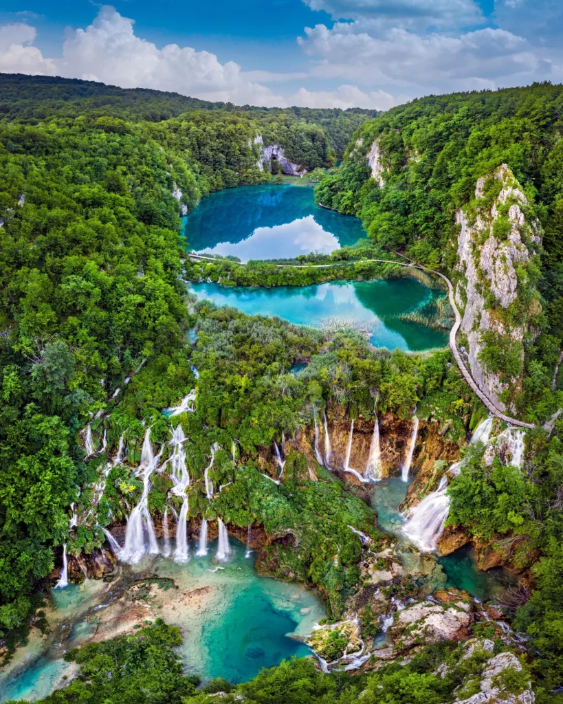 Plitvice, Kroatien - Erstaunliche Aussicht auf die wunderschönen Wasserfälle der Plitvicer Seen im Nationalpark Plitvice an einem strahlenden Sommertag mit blauem Himmel und Wolken, grünem Laub und türkisfarbenem Wasser