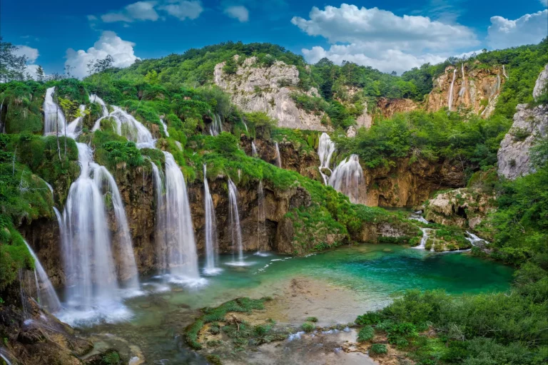 Plitvice, Croazia - Le bellissime cascate dei laghi di Plitvice (Plitvička jezera) nel Parco Nazionale di Plitvice in una luminosa giornata estiva con cielo azzurro e nuvole, fogliame verde e acqua turchese